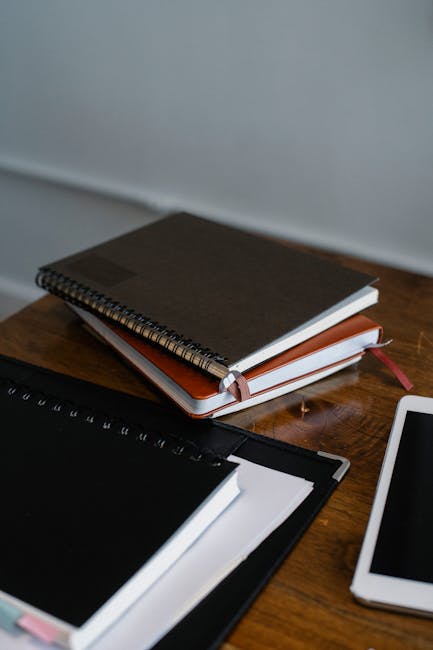 A neatly arranged workspace featuring notebooks and a digital tablet on a wooden desk.